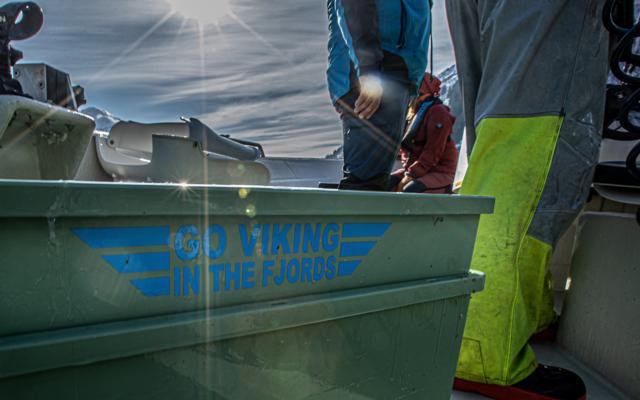 On the winter boat a green tub marked Go Viking in the Fjords stands beside guest hands and a guide in foul-weather trousers sorting rope in the low sun.