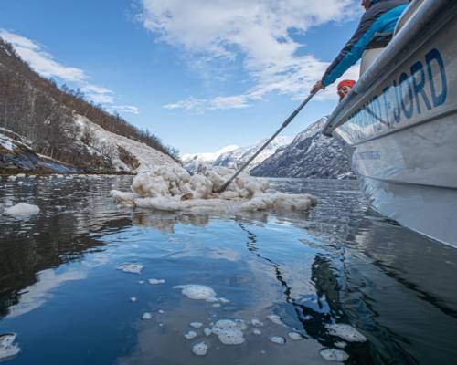 Lokal guide peker mot Naoberadn fjellside, sted for gammelt sagn, omgitt av snøflak etter et ras i hypernatur fjord