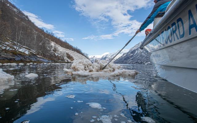 Lokal guide peker mot Naoberadn fjellside, sted for gammelt sagn, omgitt av snøflak etter et ras i hypernatur fjord