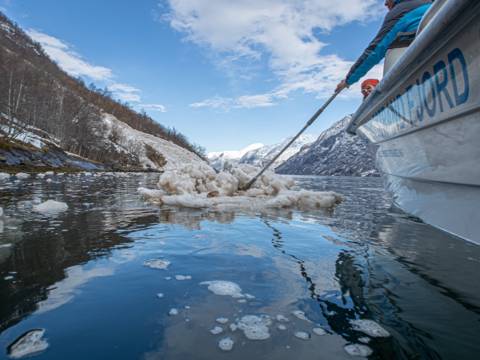 Lokal guide peker mot Naoberadn fjellside, sted for gammelt sagn, omgitt av snøflak etter et ras i hypernatur fjord