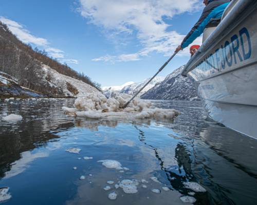 Lokal guide peker mot Naoberadn fjellside, sted for gammelt sagn, omgitt av snøflak etter et ras i hypernatur fjord