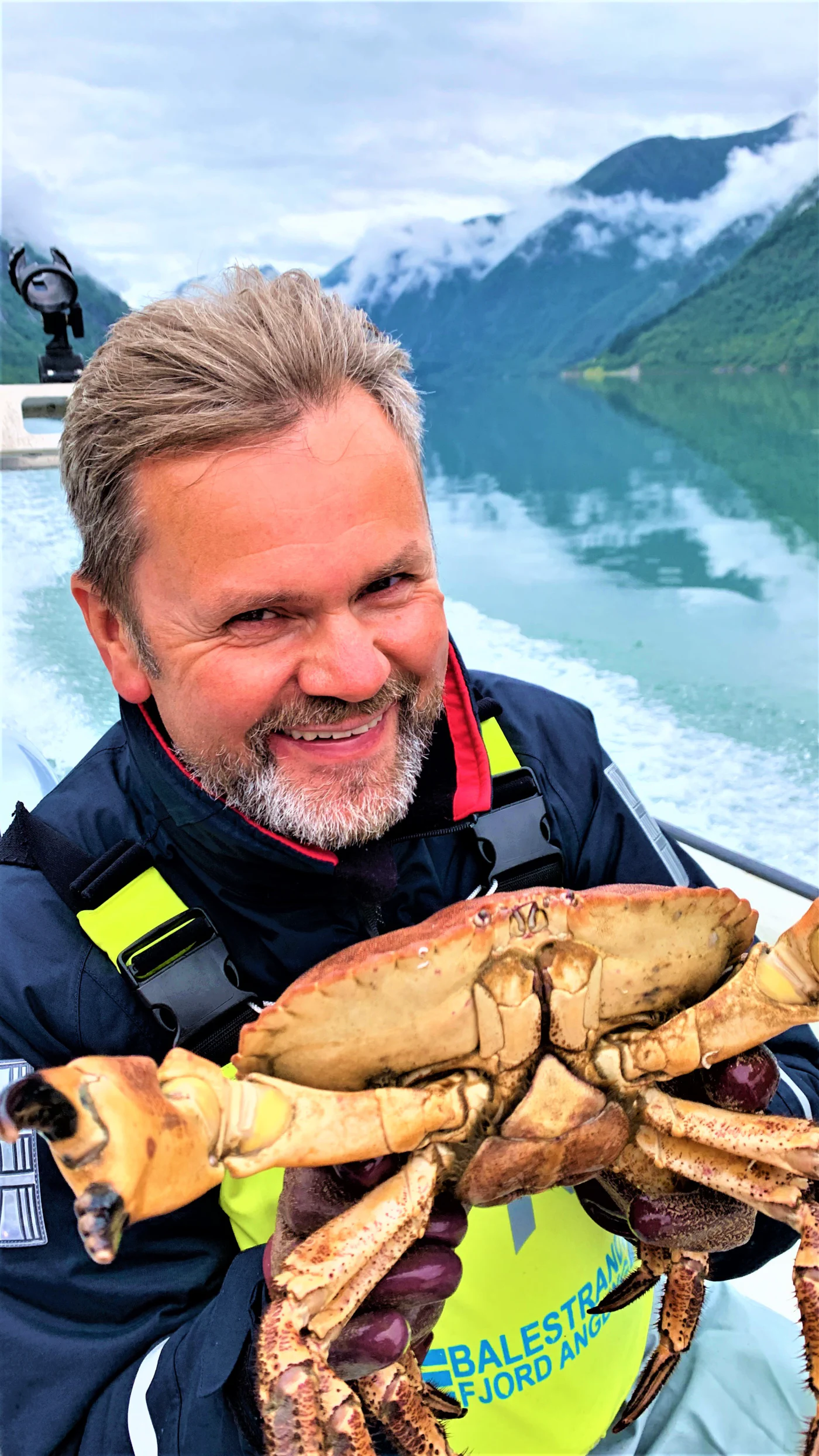 Captain Tor of Balestrand Fjord Angling showcasing a fresh brown crab, embodying 'The Human Edge' and 'Hyper-nature' in the Sognefjord. This image represents a private masterclass in authentic Norwegian fjord life, featuring sustainable harvesting, local expertise, and the serene, misty mountains of Balestrand in the background.