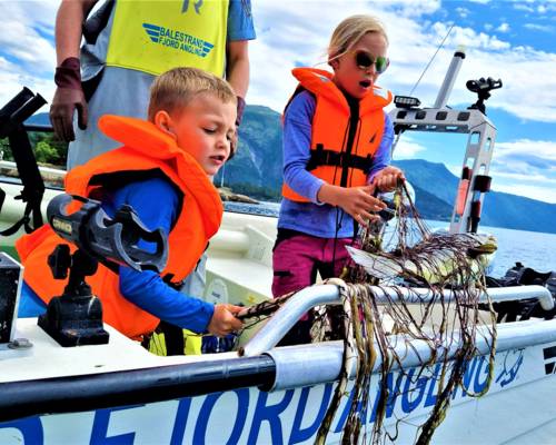 "Children learning traditional gillnet fishing in Balestrand, Norway, with Captain Tor. Kids discovering a fresh catch in the net on a boat in the Sognefjord." 
