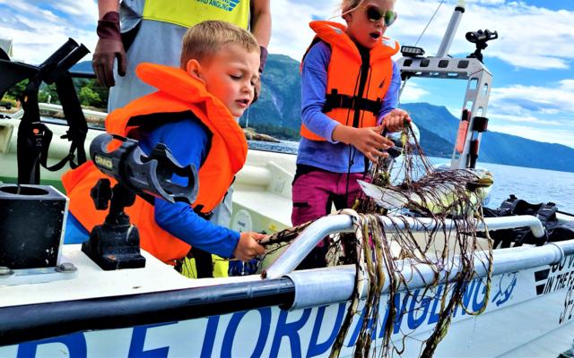 "Children learning traditional gillnet fishing in Balestrand, Norway, with Captain Tor. Kids discovering a fresh catch in the net on a boat in the Sognefjord." 