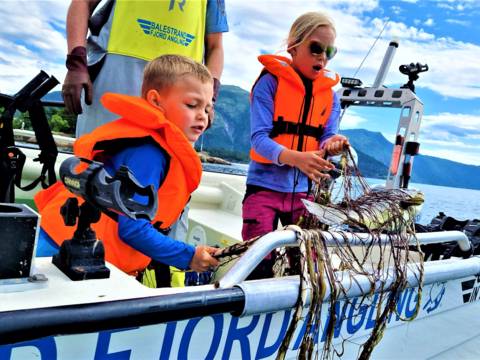"Children learning traditional gillnet fishing in Balestrand, Norway, with Captain Tor. Kids discovering a fresh catch in the net on a boat in the Sognefjord." 