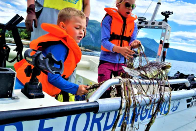 "Children learning traditional gillnet fishing in Balestrand, Norway, with Captain Tor. Kids discovering a fresh catch in the net on a boat in the Sognefjord." 