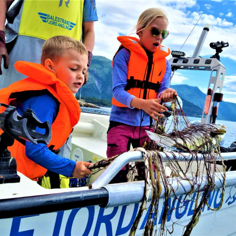 "Children learning traditional gillnet fishing in Balestrand, Norway, with Captain Tor. Kids discovering a fresh catch in the net on a boat in the Sognefjord." 