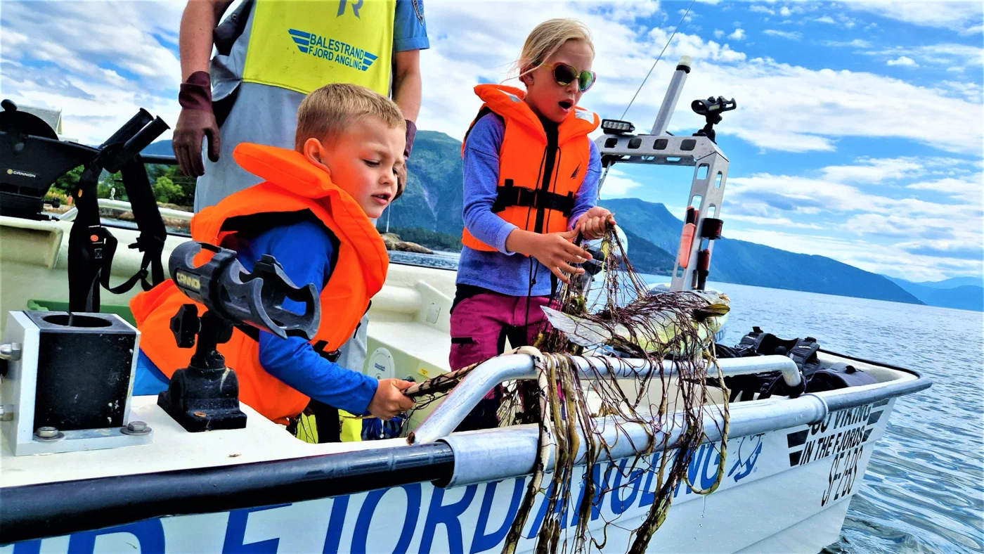 "Children learning traditional gillnet fishing in Balestrand, Norway, with Captain Tor. Kids discovering a fresh catch in the net on a boat in the Sognefjord."