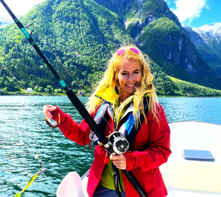 smiling woman with fishing rod and red jacket fishing in Esefjorden Norway with captain Tor among high mountains in Sognefjorden