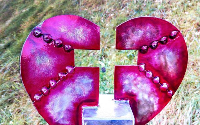 A close-up of a red-painted metal sculpture on a steel post in the grass.