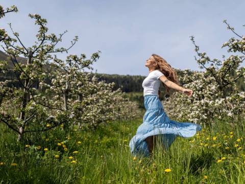 Woman dancing joyfully in a blossoming apple orchard in Balestrand, Sognefjord. The image captures the Norwegian 'springfulness' feeling, mental wellness, and authentic nature experience.