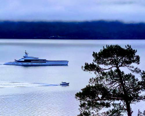 Superyacht 'Bravo Eugenia' next to a small boat in the Sognefjord, illustrating 3D luxury versus 5D authentic experience.